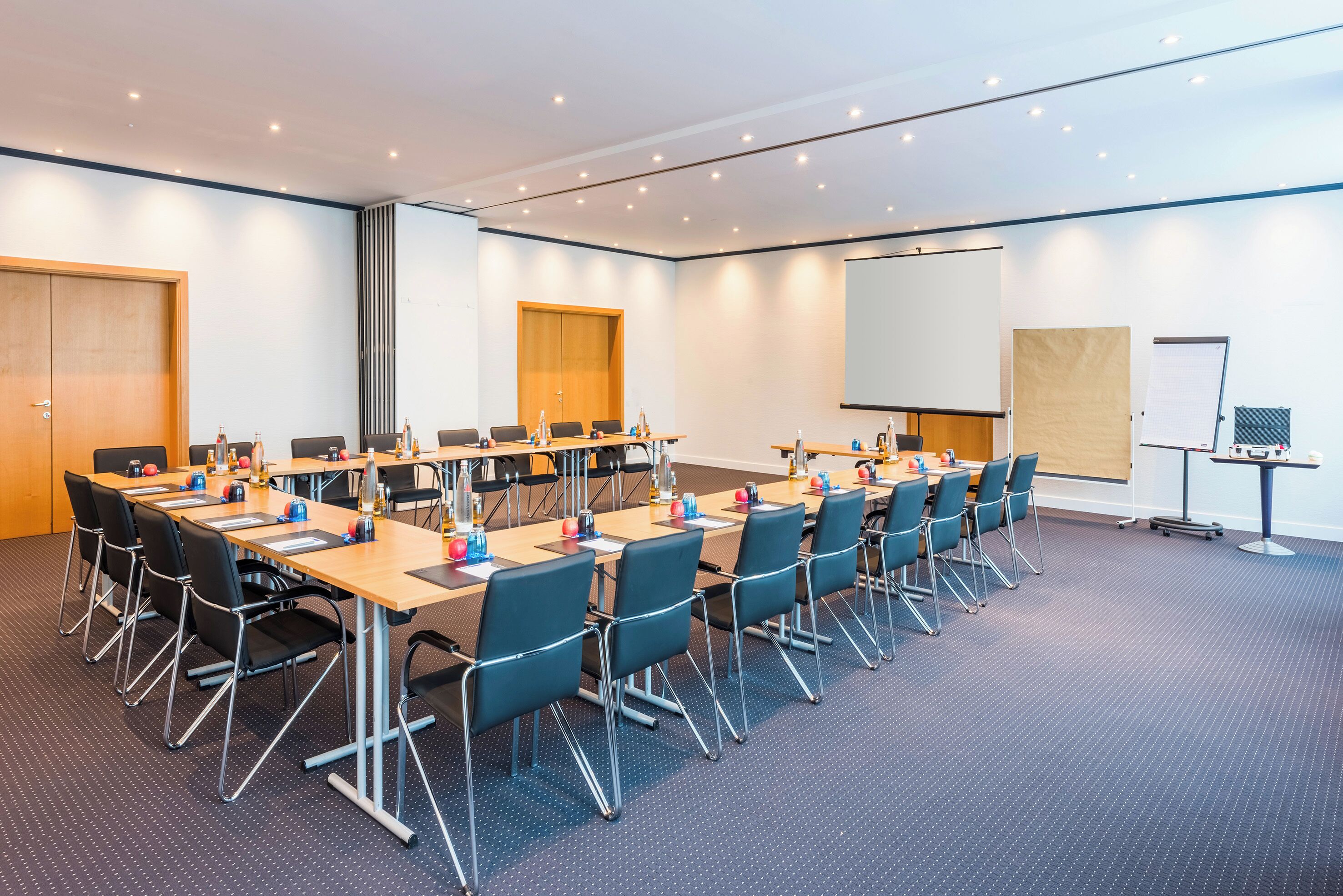 Ein Konferenzraum mit mehreren Tischen und Stühlen, einer Projektionsleinwand und einer Whiteboard-Tafel.