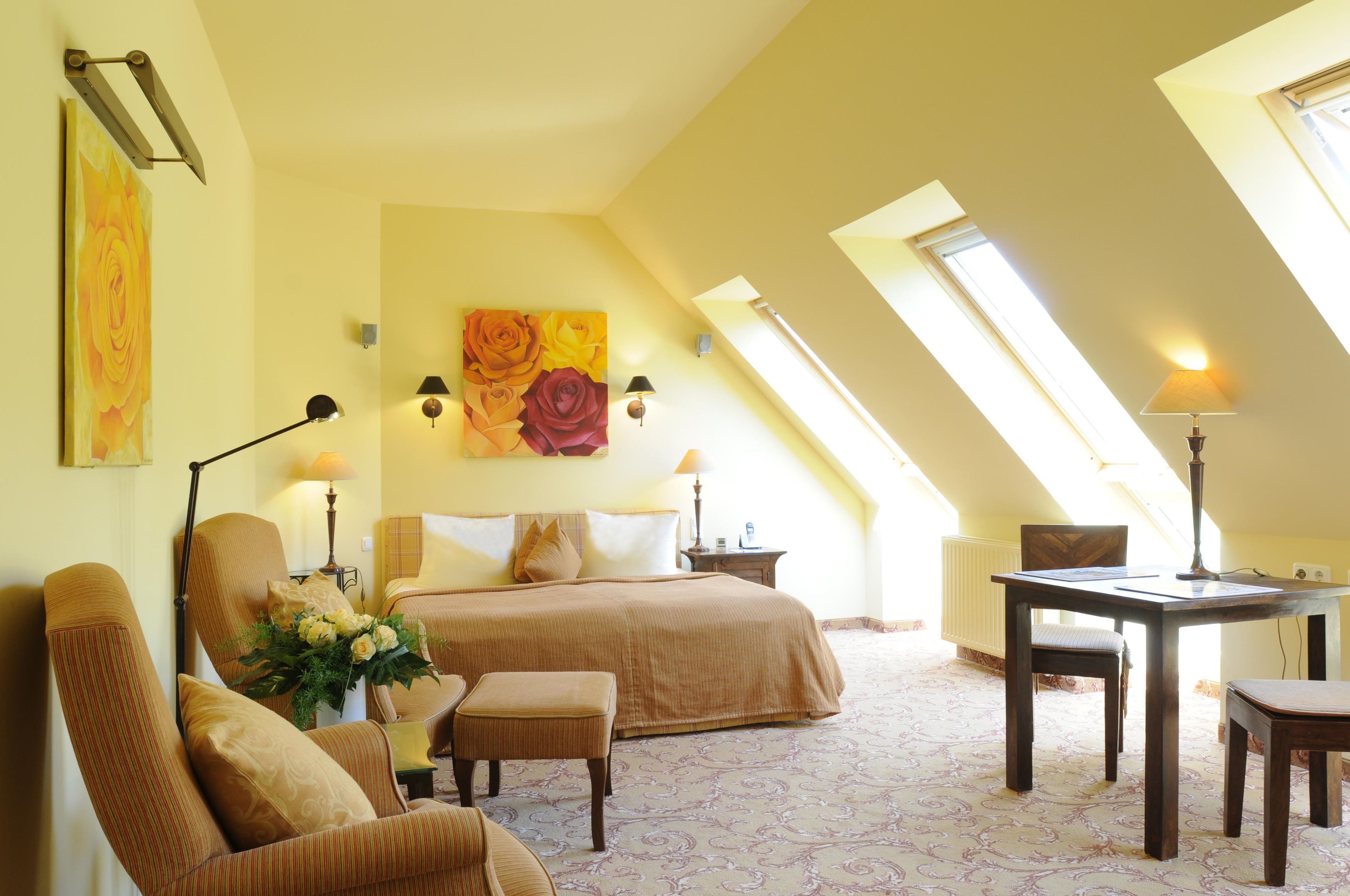 A room with a bed, a desk, and a chair. There are two lamps on the desk and a painting on the wall.