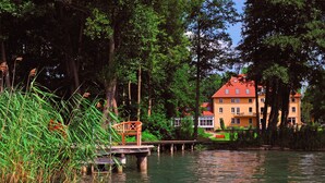 A riverside view with a wooden bridge and a building with a red roof. - Seehotel Frankenhorst - BW Signature Collection (Schwerin)