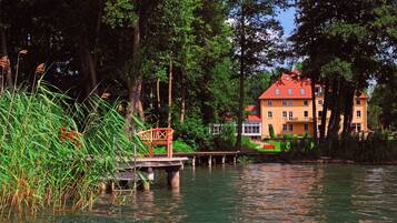 A riverside view with a wooden bridge and a building with a red roof.