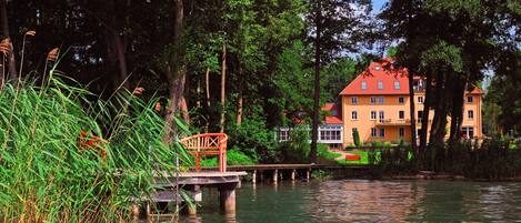 A riverside view with a wooden bridge and a building with a red roof.