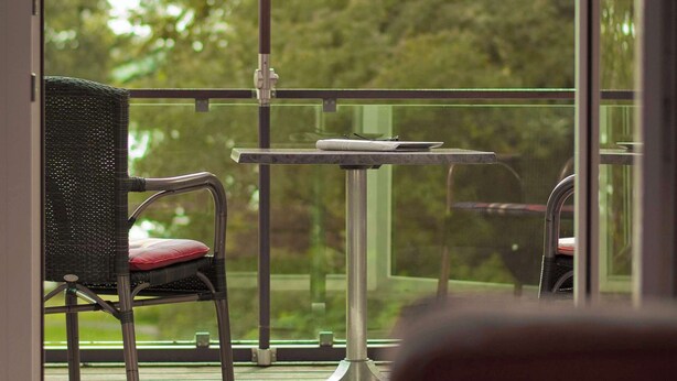 A balcony with a red umbrella, a chair, and a table. - Seehotel Frankenhorst - BW Signature Collection (Schwerin)