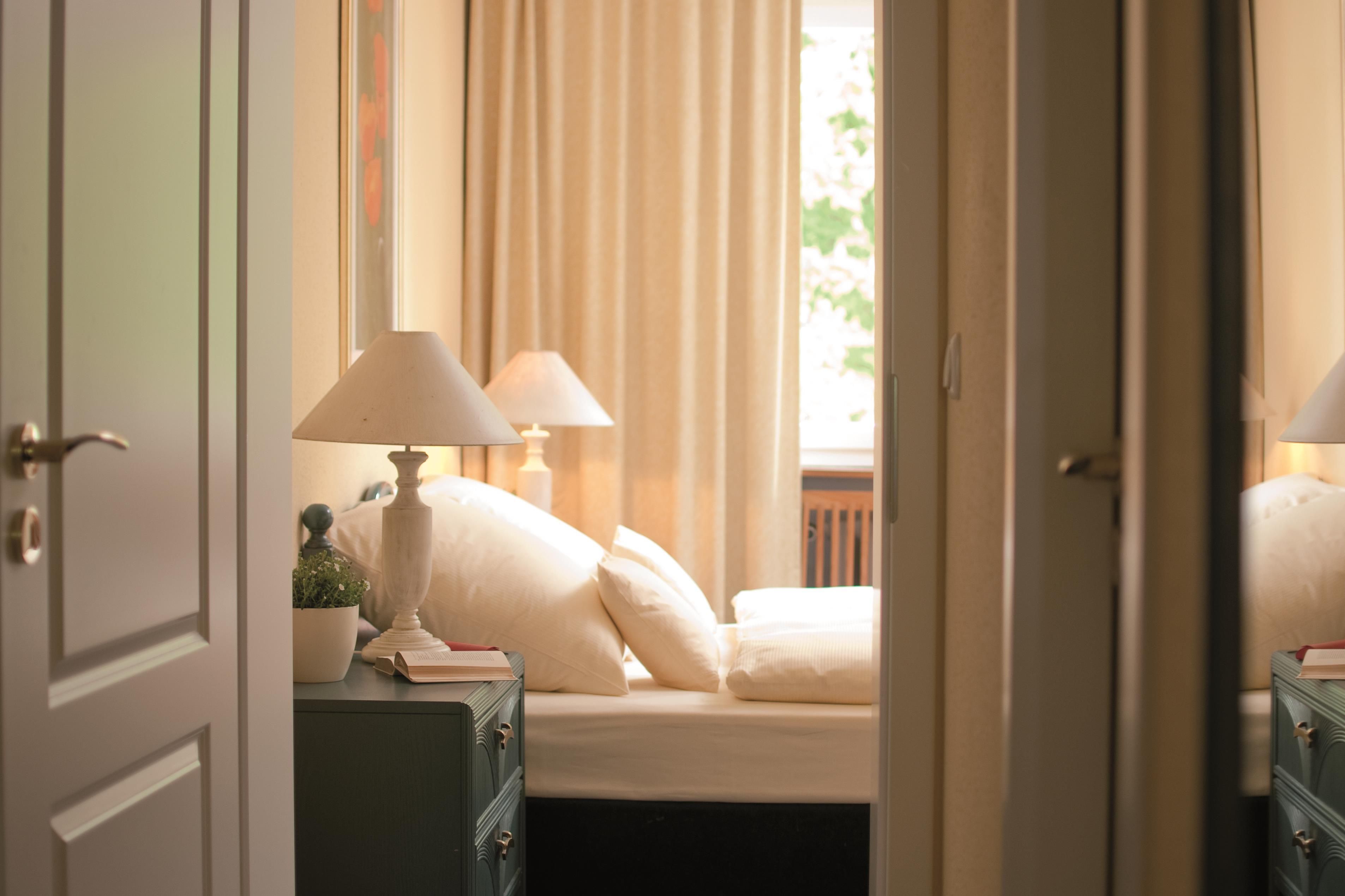 Quarto com uma cama, duas luminárias de cabeceira, uma mesa de cabeceira com abajur e uma janela com cortinas.