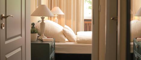 Quarto com uma cama, duas luminárias de cabeceira, uma mesa de cabeceira com abajur e uma janela com cortinas.