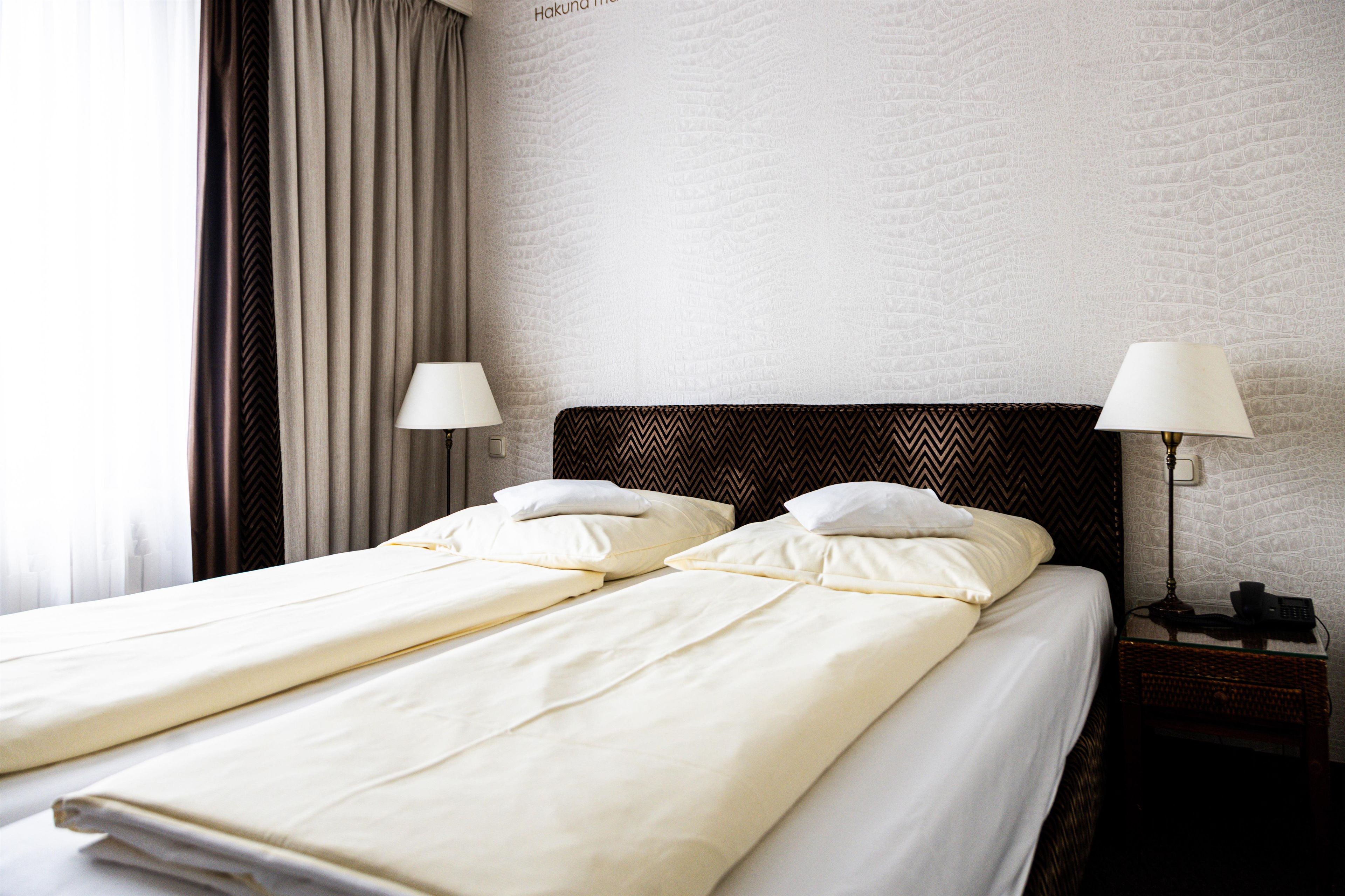 Un lit double avec deux oreillers, une table de chevet avec une lampe et un mur orné d’un motif texturé.