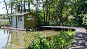 A wooden sauna structure labeled "SEE SAUNA" adjacent to a pond, surrounded by lush greenery and a wooden boardwalk. - Seehotel Frankenhorst - BW Signature Collection (Schwerin)