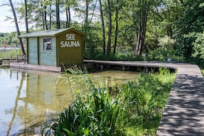 A wooden sauna structure labeled "SEE SAUNA" adjacent to a pond, surrounded by lush greenery and a wooden boardwalk. - Seehotel Frankenhorst - BW Signature Collection (Schwerin)
