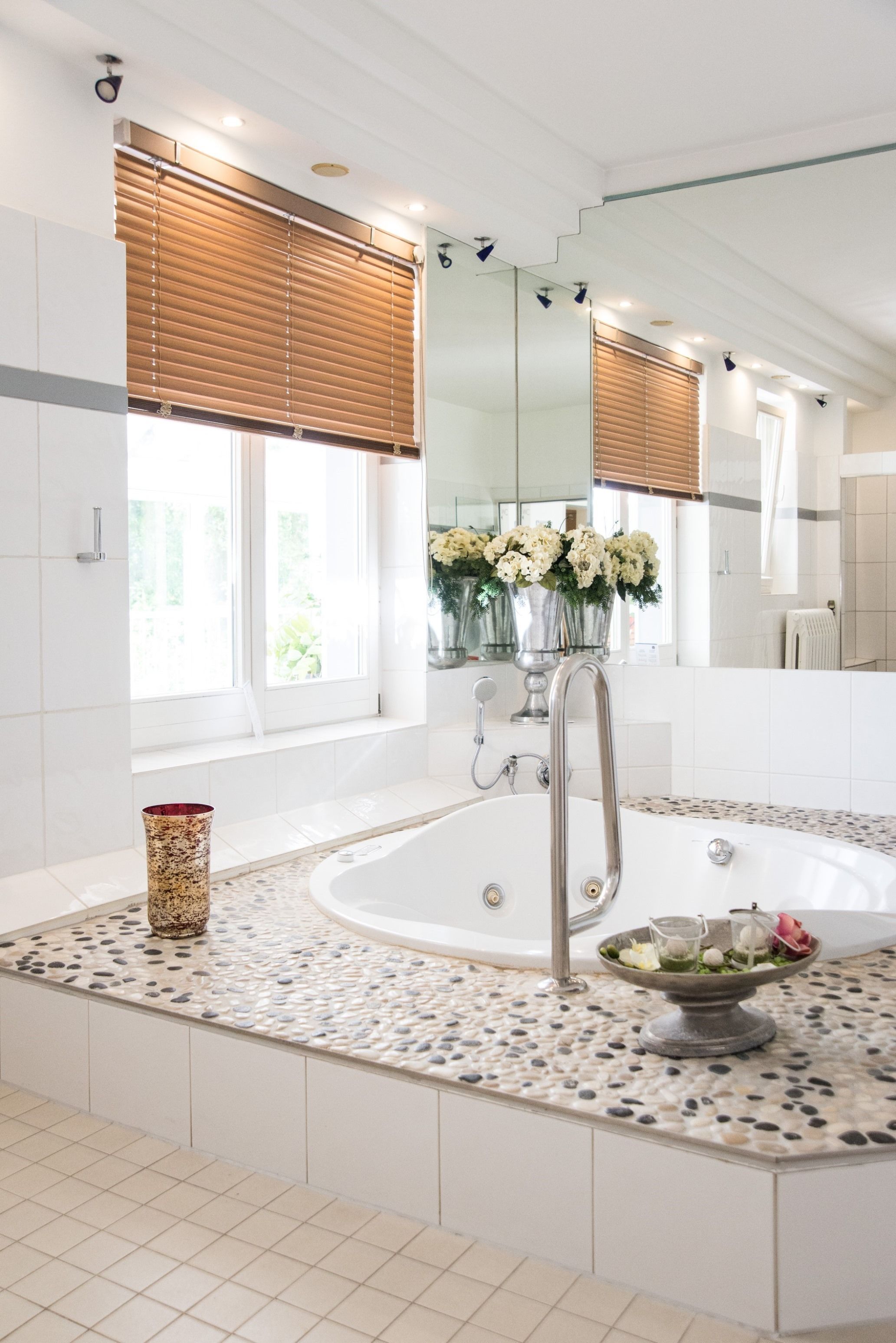 A modern bathroom with a freestanding bathtub, a large mirror, and a window with blinds.
