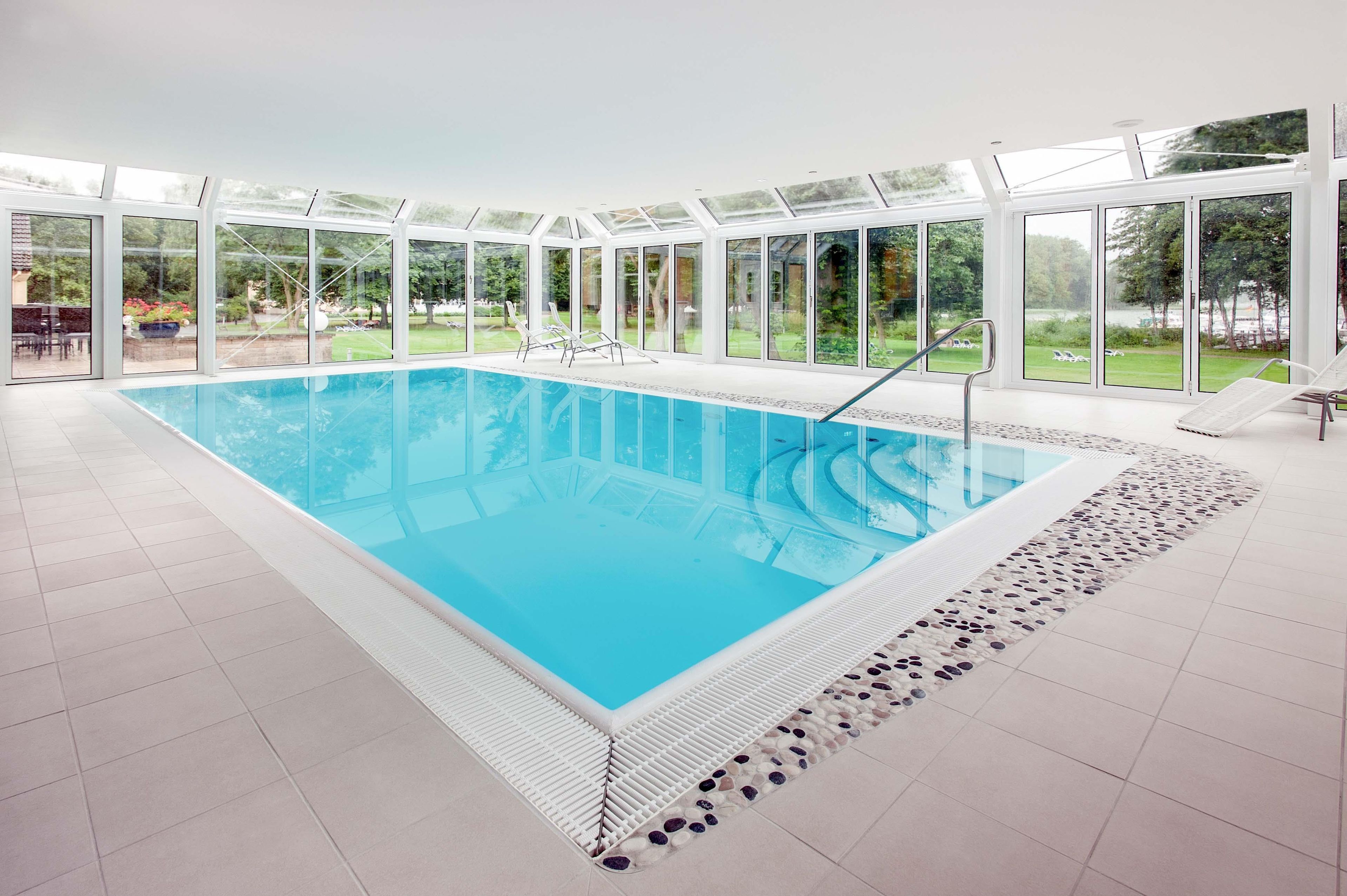 Una amplia piscina interior con paredes de vidrio transparente, rodeada por un piso de baldosas y un borde de guijarros.