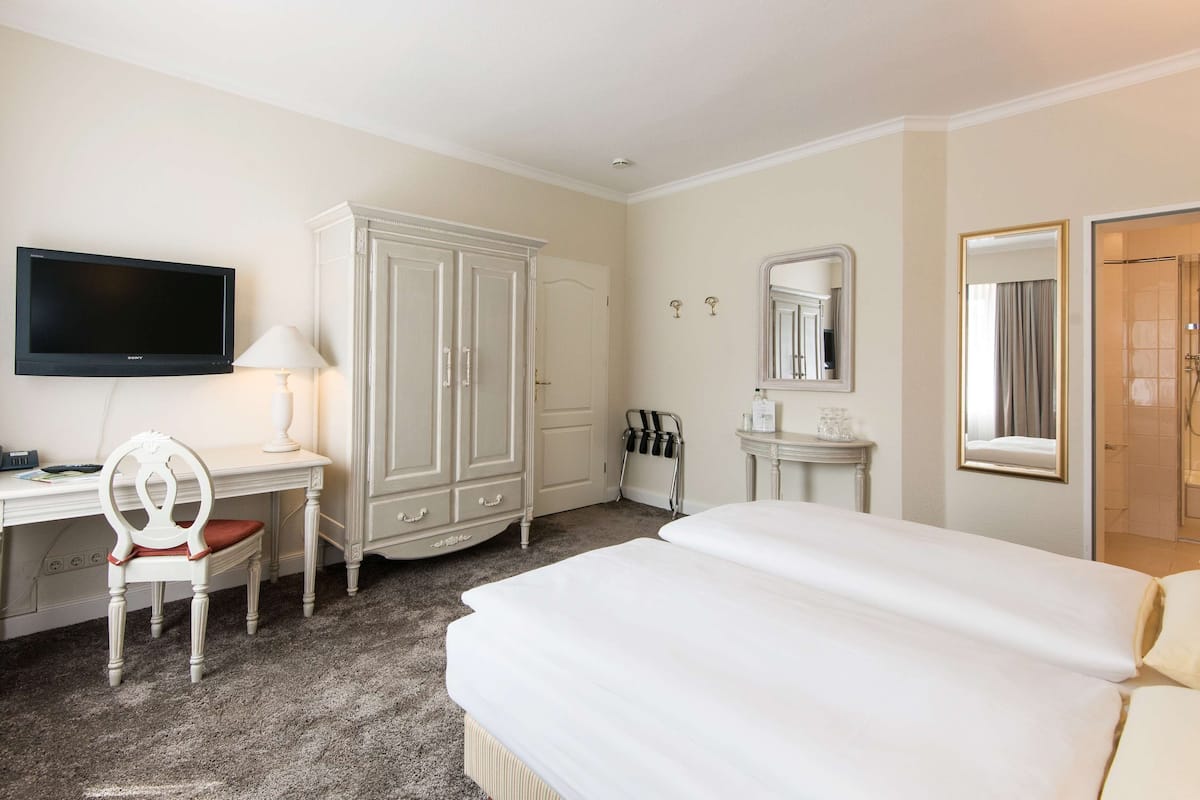 A hotel room with a bed, a desk with a chair, a television, a wardrobe, a mirror, and a bathroom door.