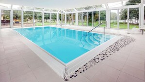 Une piscine intérieure avec des parois en verre transparent, un sol carrelé et un bord en petits galets.