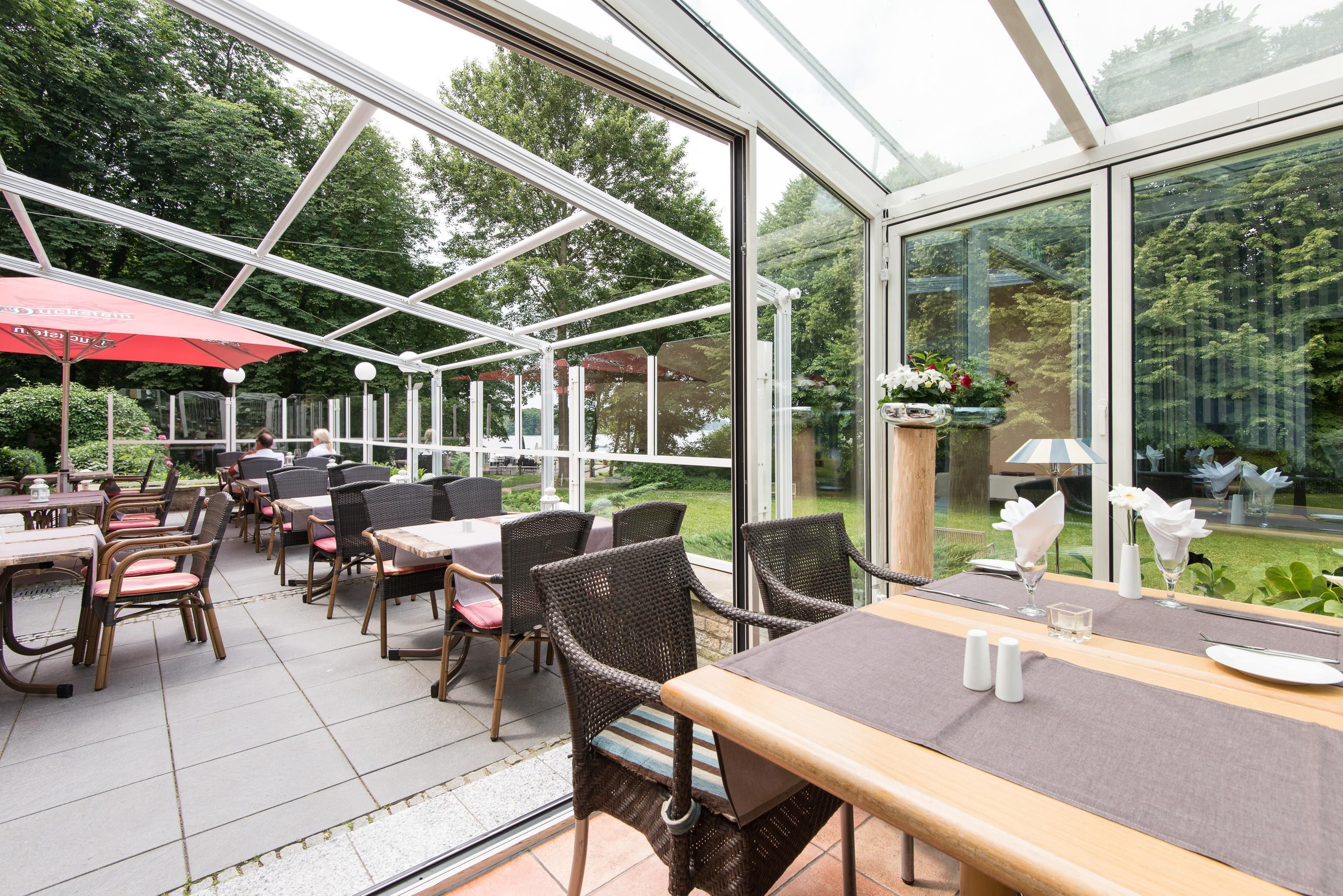 Un café en plein air avec des tables et des chaises, de grandes fenêtres et une structure de toit en verre.