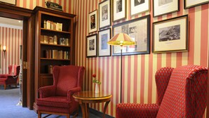 A room with striped wallpaper, a bookshelf, two patterned armchairs, a small table with a vase, and a floor lamp. - Seehotel Frankenhorst - BW Signature Collection (Schwerin)