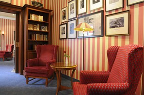 A room with striped wallpaper, a bookshelf, two patterned armchairs, a small table with a vase, and a floor lamp. - Seehotel Frankenhorst - BW Signature Collection (Schwerin)