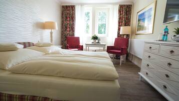 A hotel room with a large bed, two red chairs, a small table, a dresser, and a window with curtains.