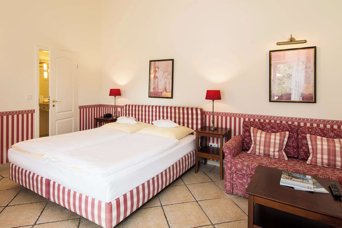 A hotel room with a large bed, a sofa, two lamps, and two framed pictures on the wall.
