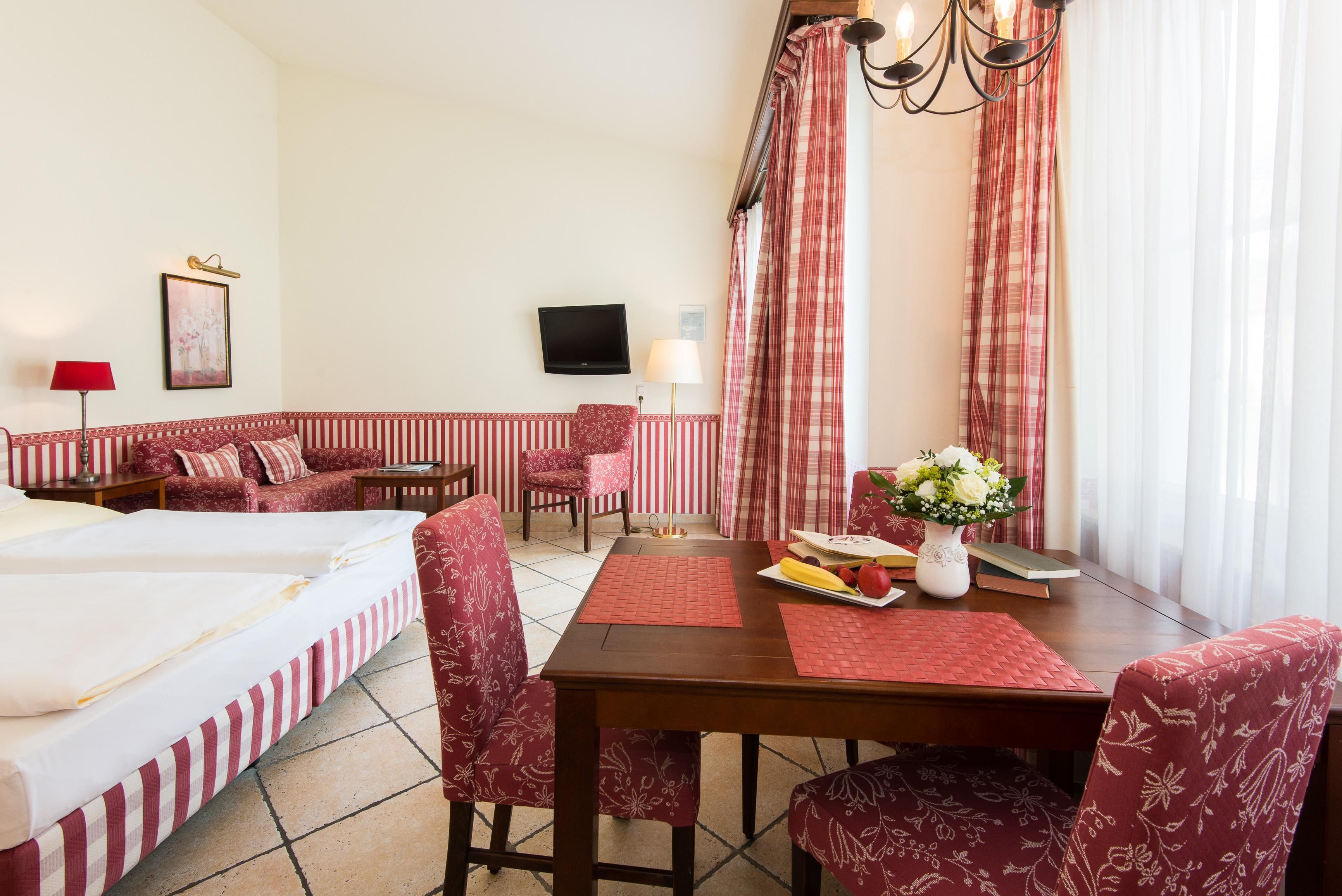 A hotel room with a bed, a sofa, a dining table, and a TV.