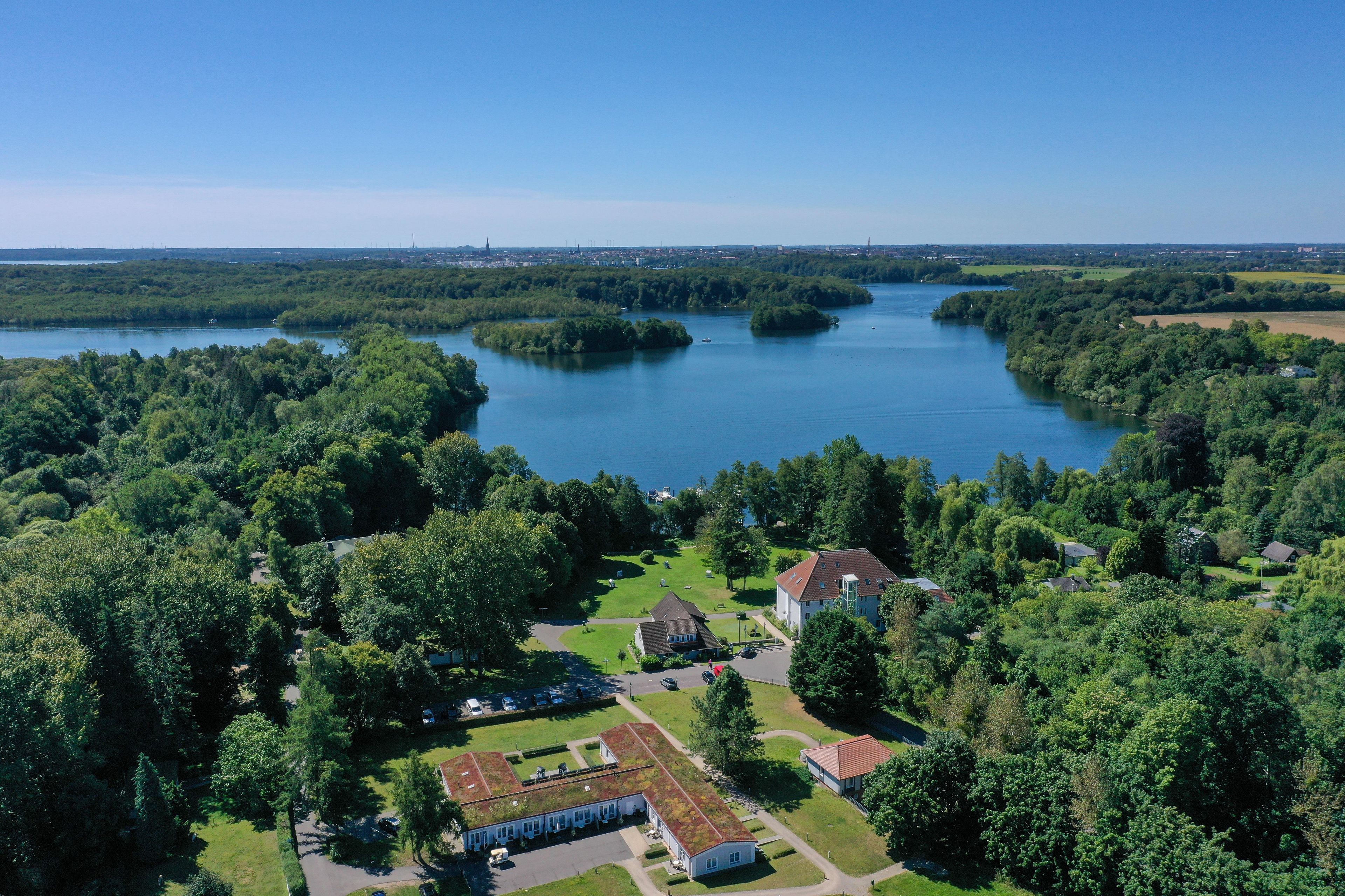 An aerial view of a lakeside property with a large building, a parking area, and surrounding greenery.