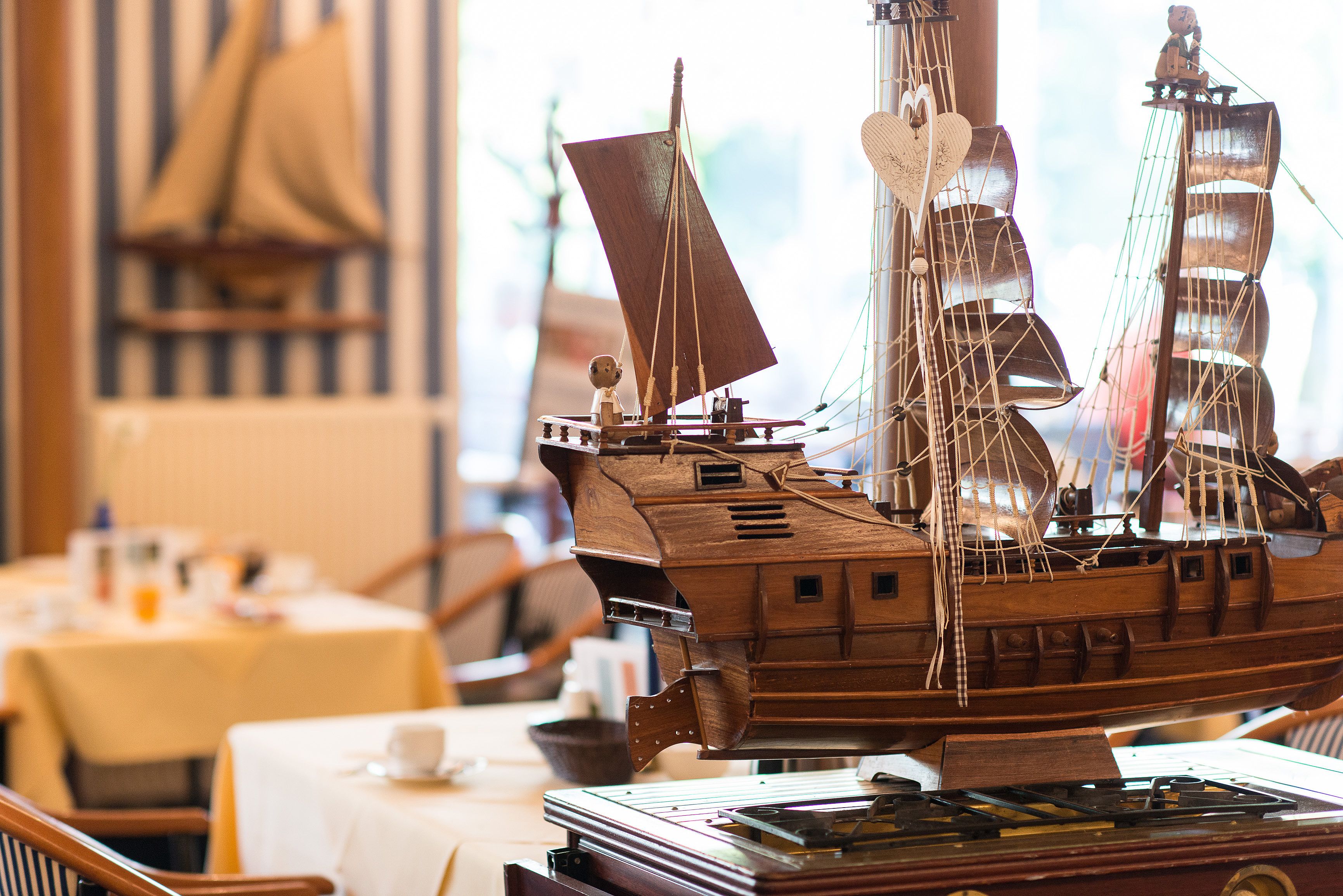 A detailed wooden ship model displayed prominently in a room with tables and chairs, suggesting a historical or nautical theme.