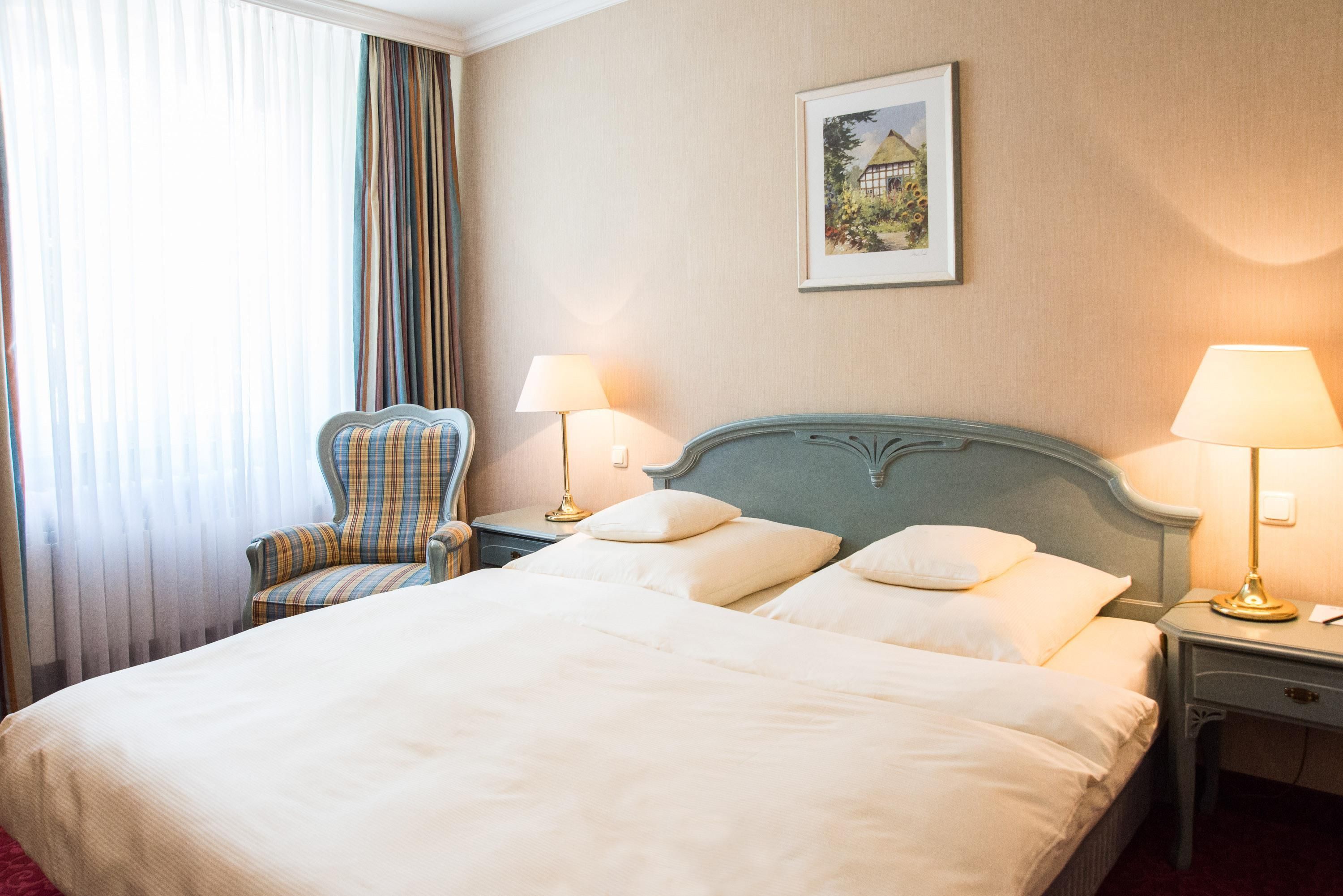 Een hotelkamer met een bed, twee bedlampen, een stoel en een schilderij aan de muur.
