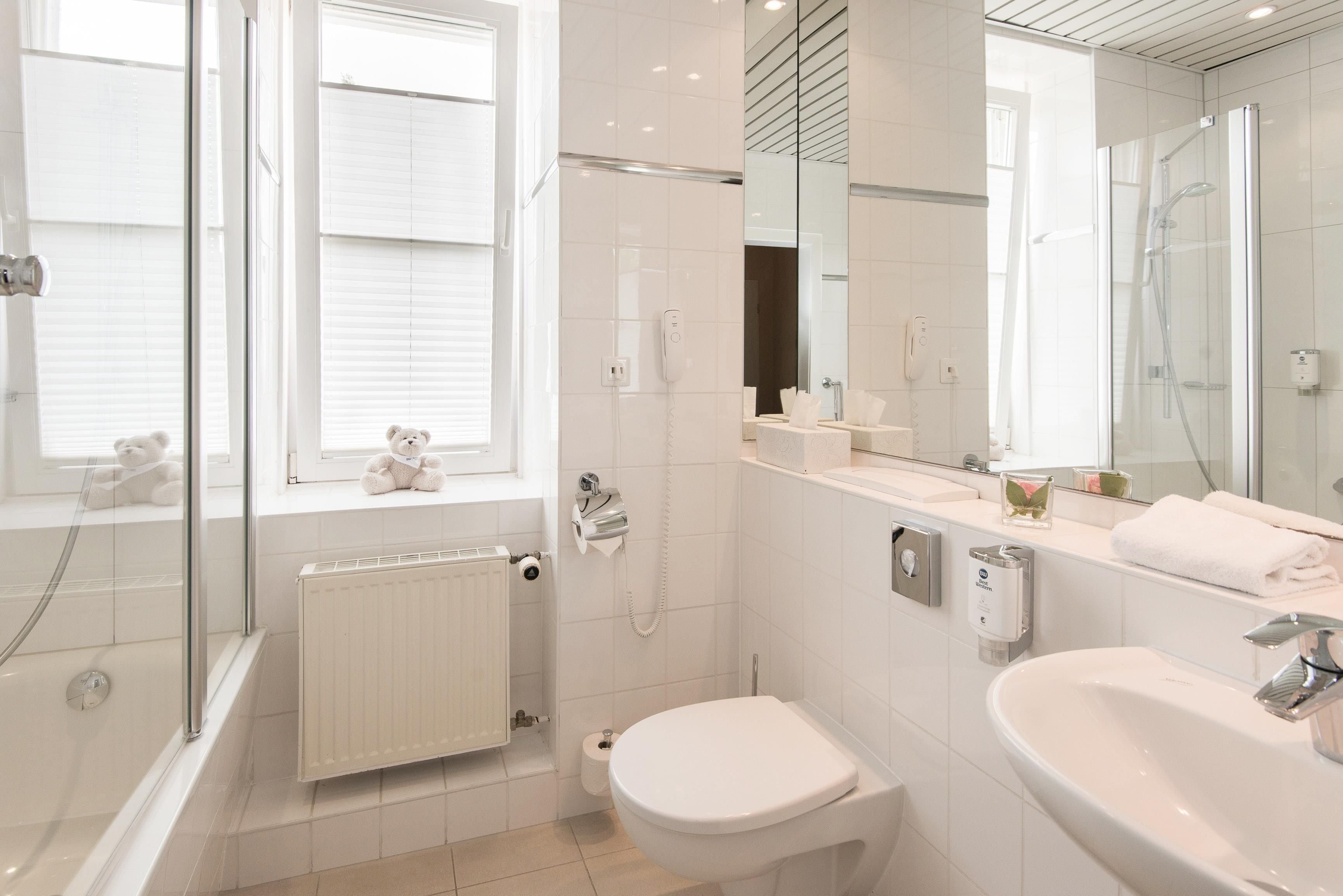 A modern bathroom with a glass shower enclosure, a toilet, a sink, and a window with blinds.