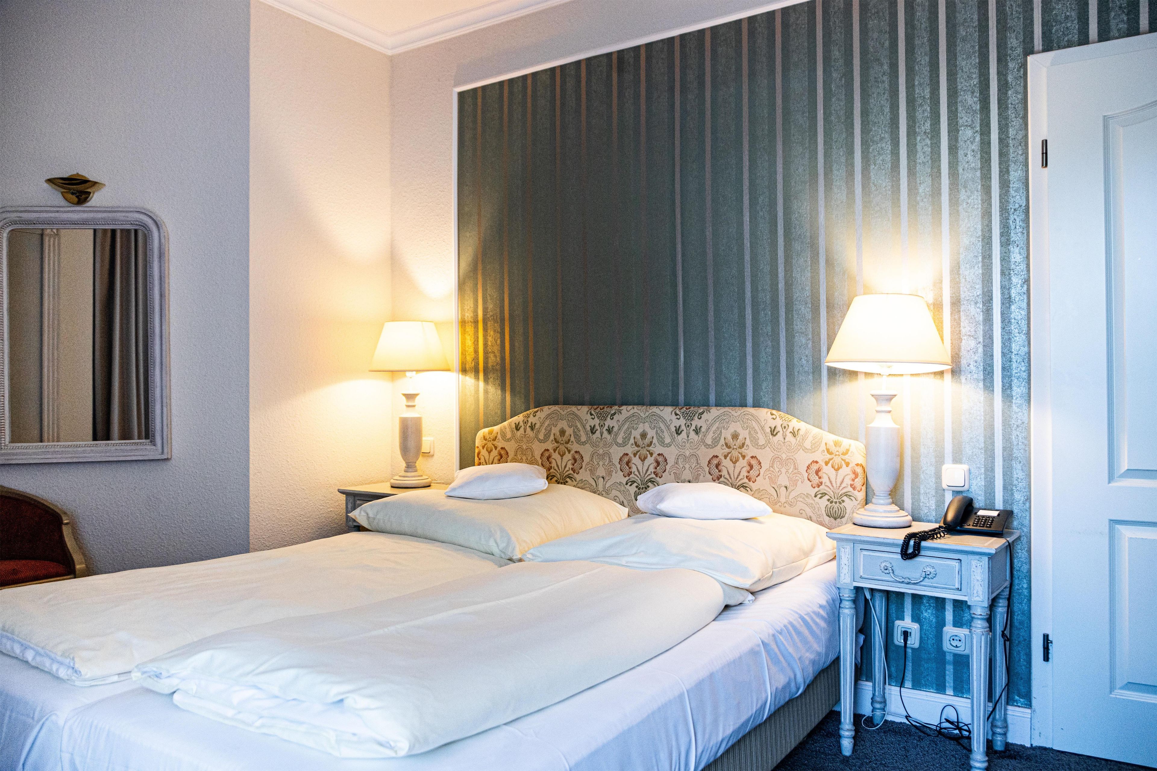 A neatly made bed with pillows, a bedside lamp, a telephone, and a wall-mounted mirror.
