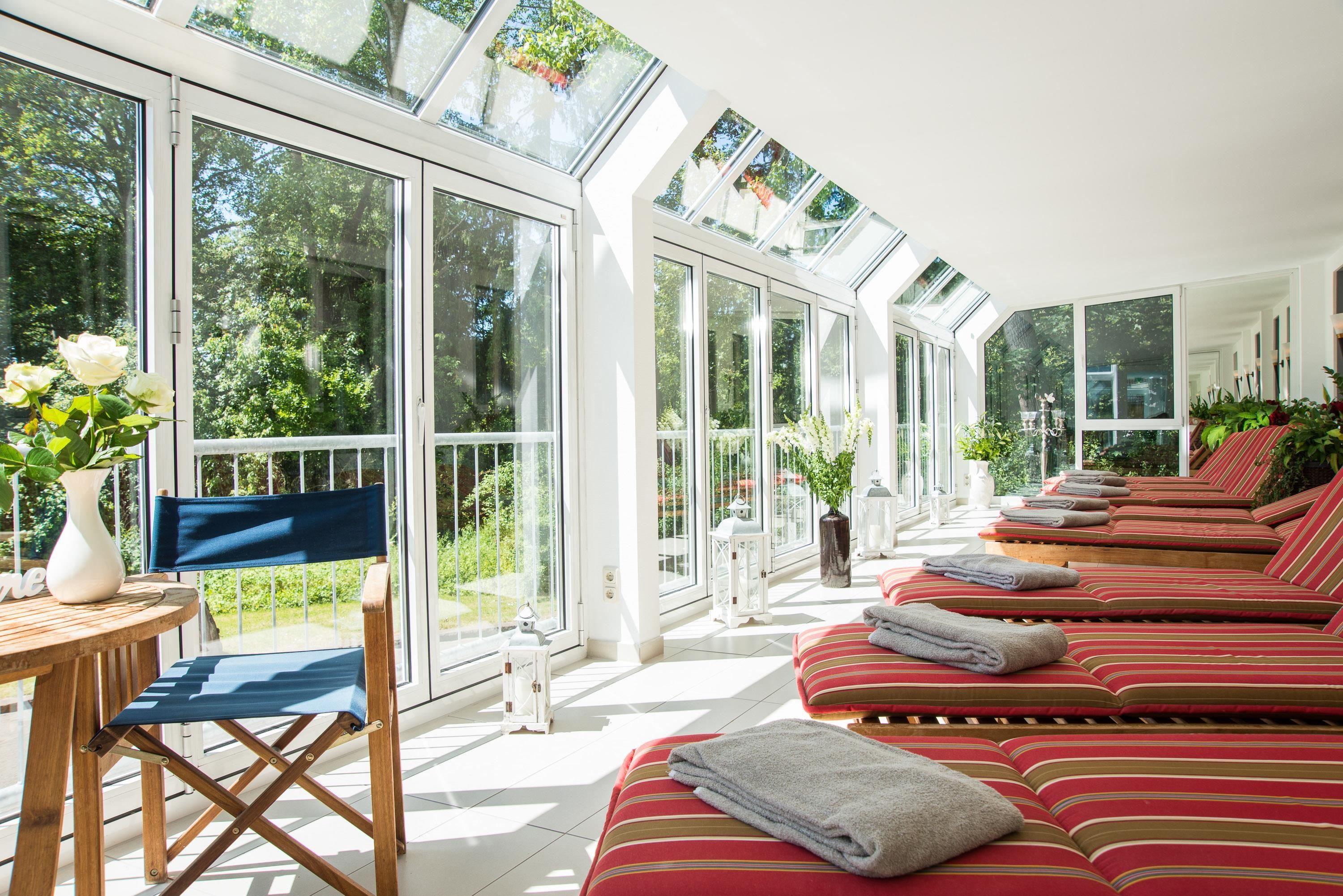 Una habitación soleada con ventanas amplias, una zona de estar con cojines a rayas y una pequeña mesa con un florero.