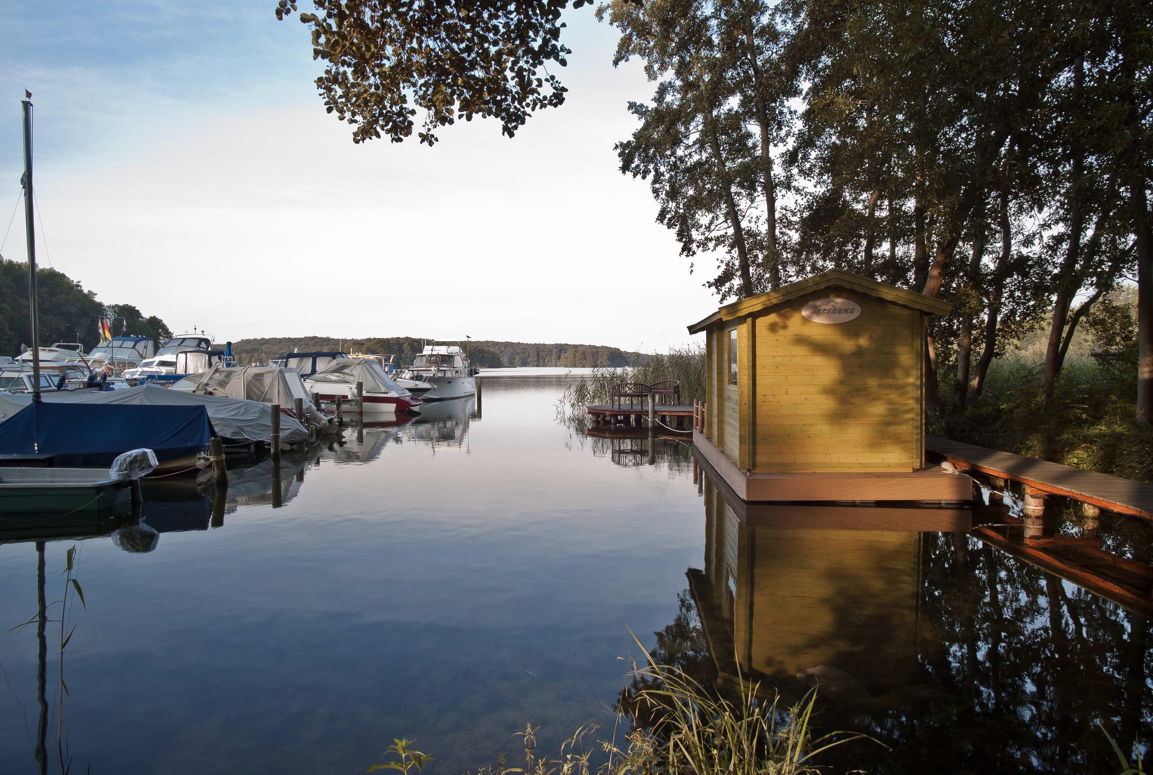 A calm marina with boats docked, a wooden boathouse, and a clear sky.