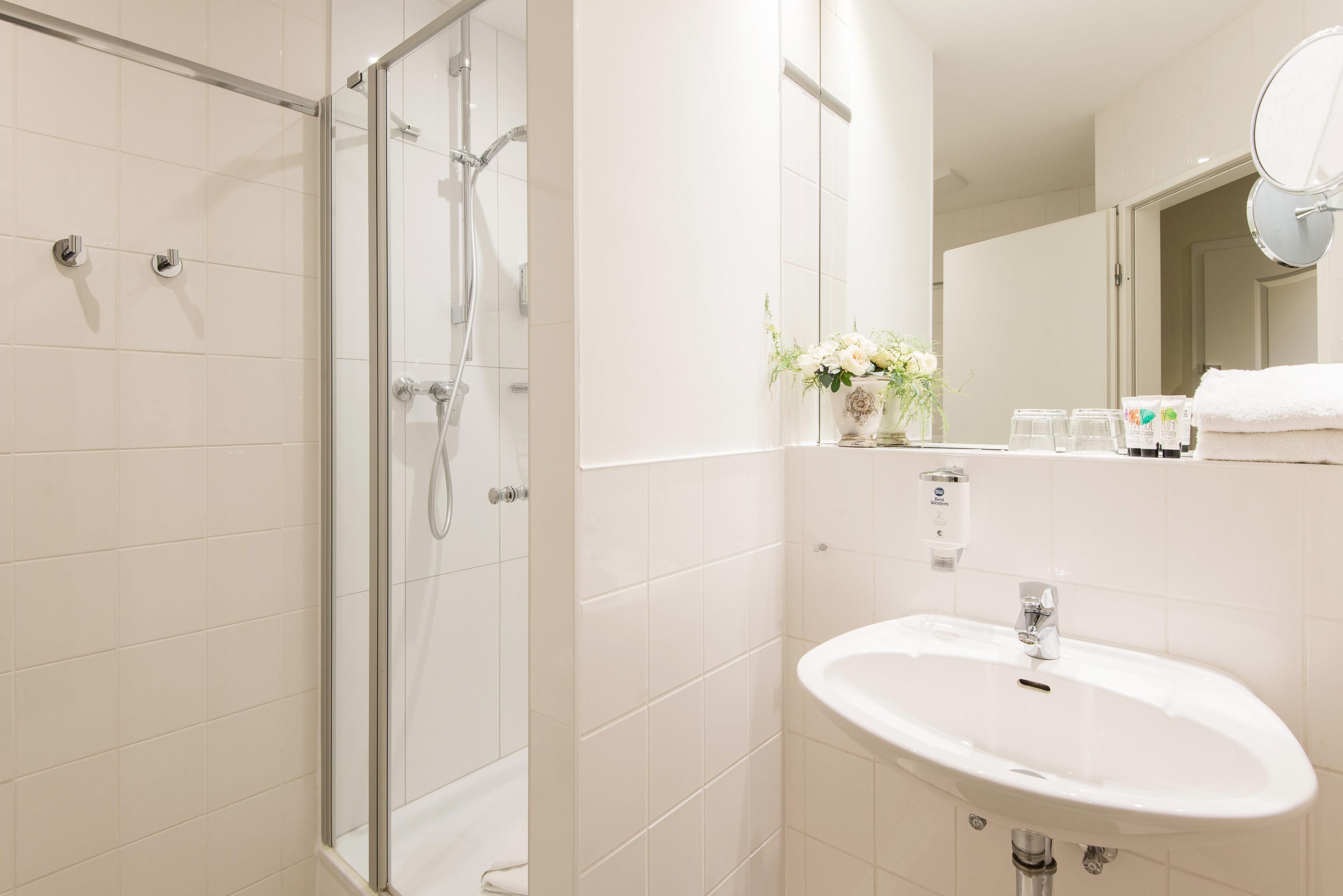 Un baño moderno con ducha envuelta en vidrio, un lavabo blanco y un espejo sobre él.