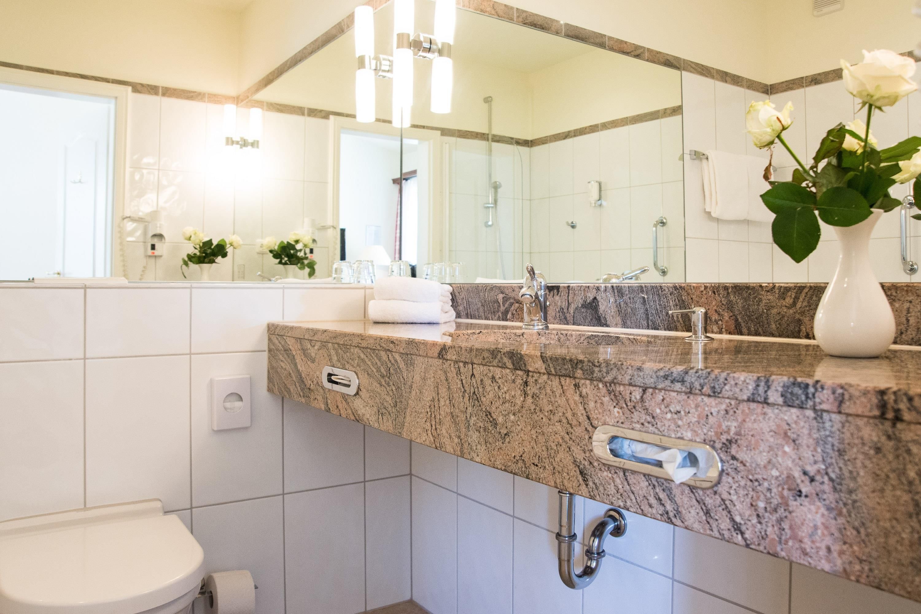 A modern bathroom with a marble countertop, a sink, a mirror, and a toilet.