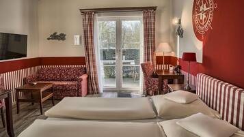 Habitación de hotel con cama, sofá, sillón, televisor y puerta corrediza de vidrio al exterior.