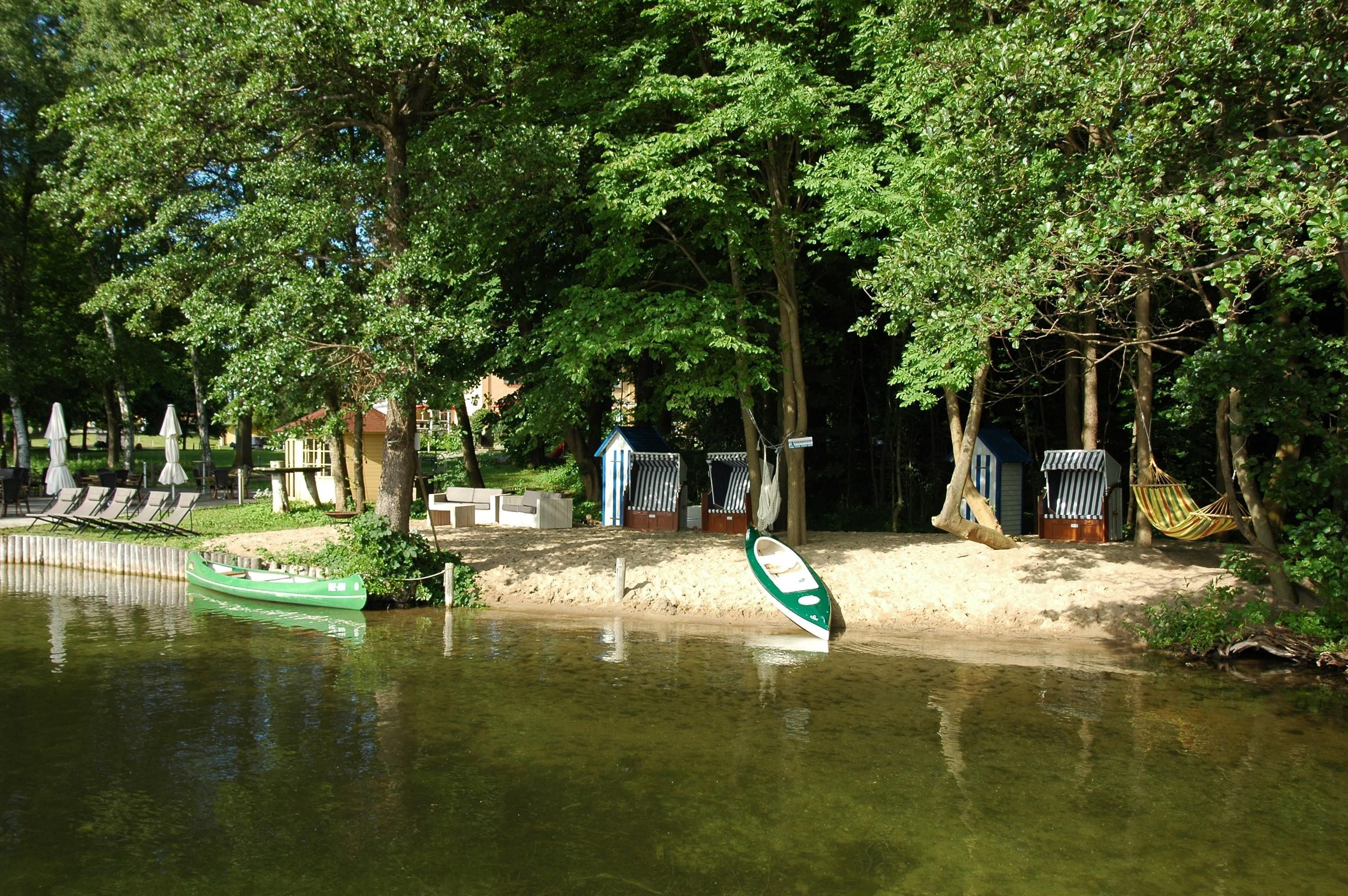 Una zona junto al río con un bote verde, sillas de descanso y un edificio pequeño.