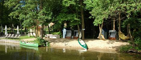 A riverside area with a green boat, lounge chairs, and a small building.