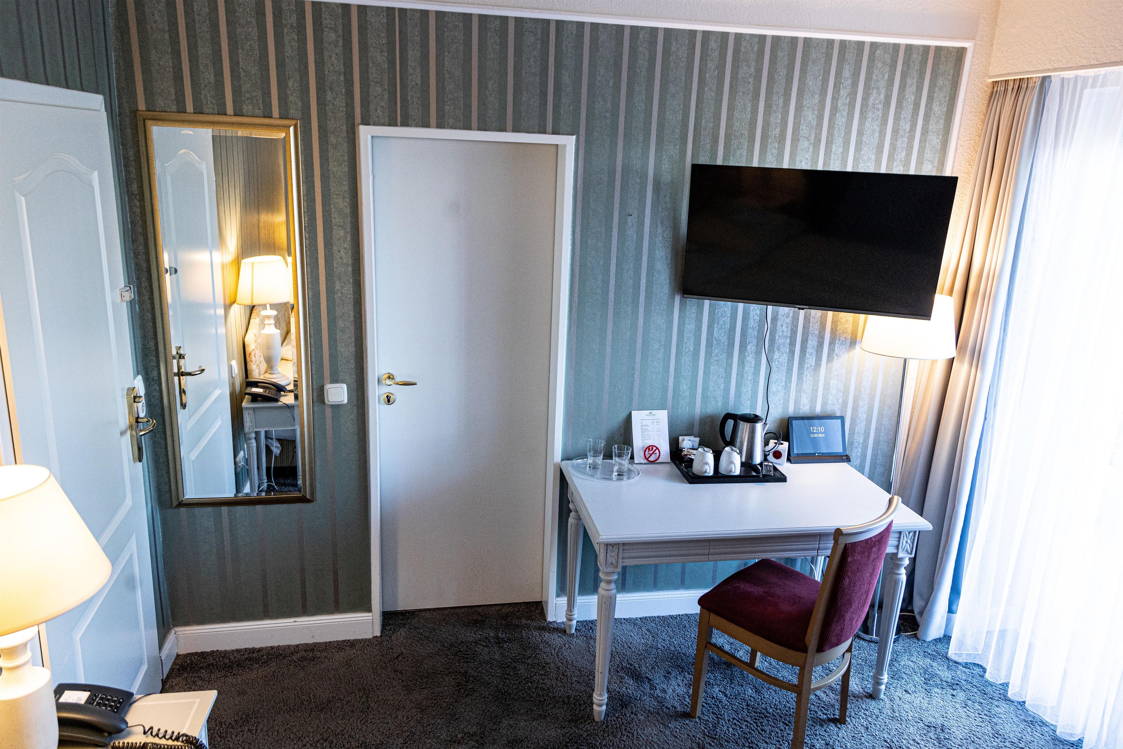 Una habitación de hotel con una cama, un escritorio, una silla, un televisor, un espejo y una ventana.