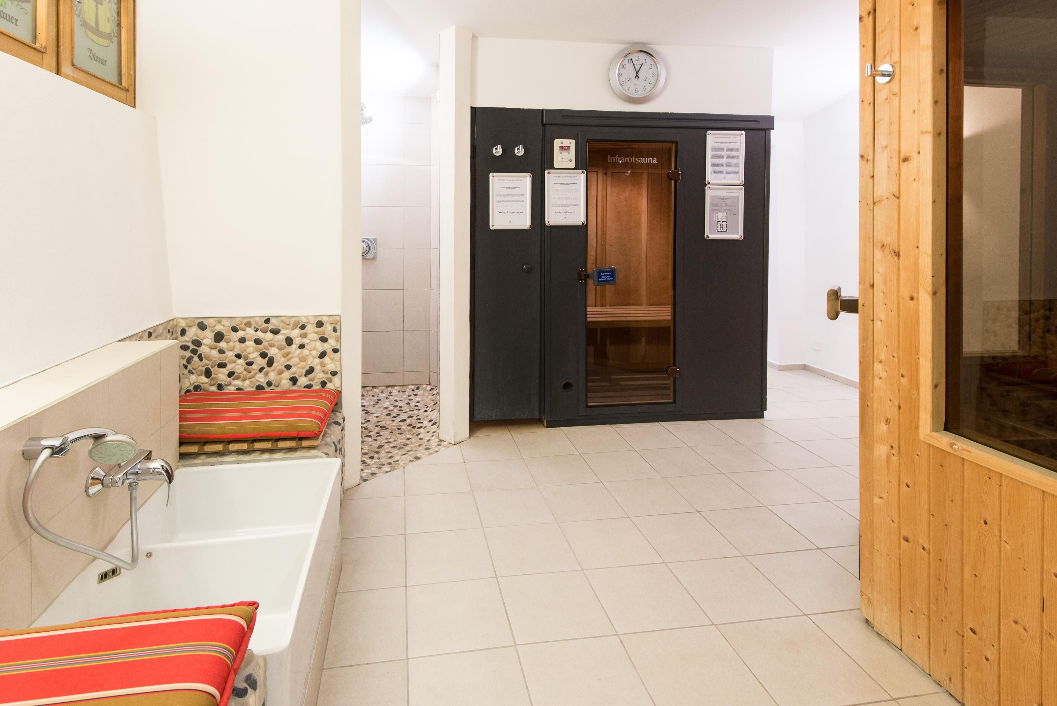 A bathroom with a bathtub, a shower, and a sauna door.