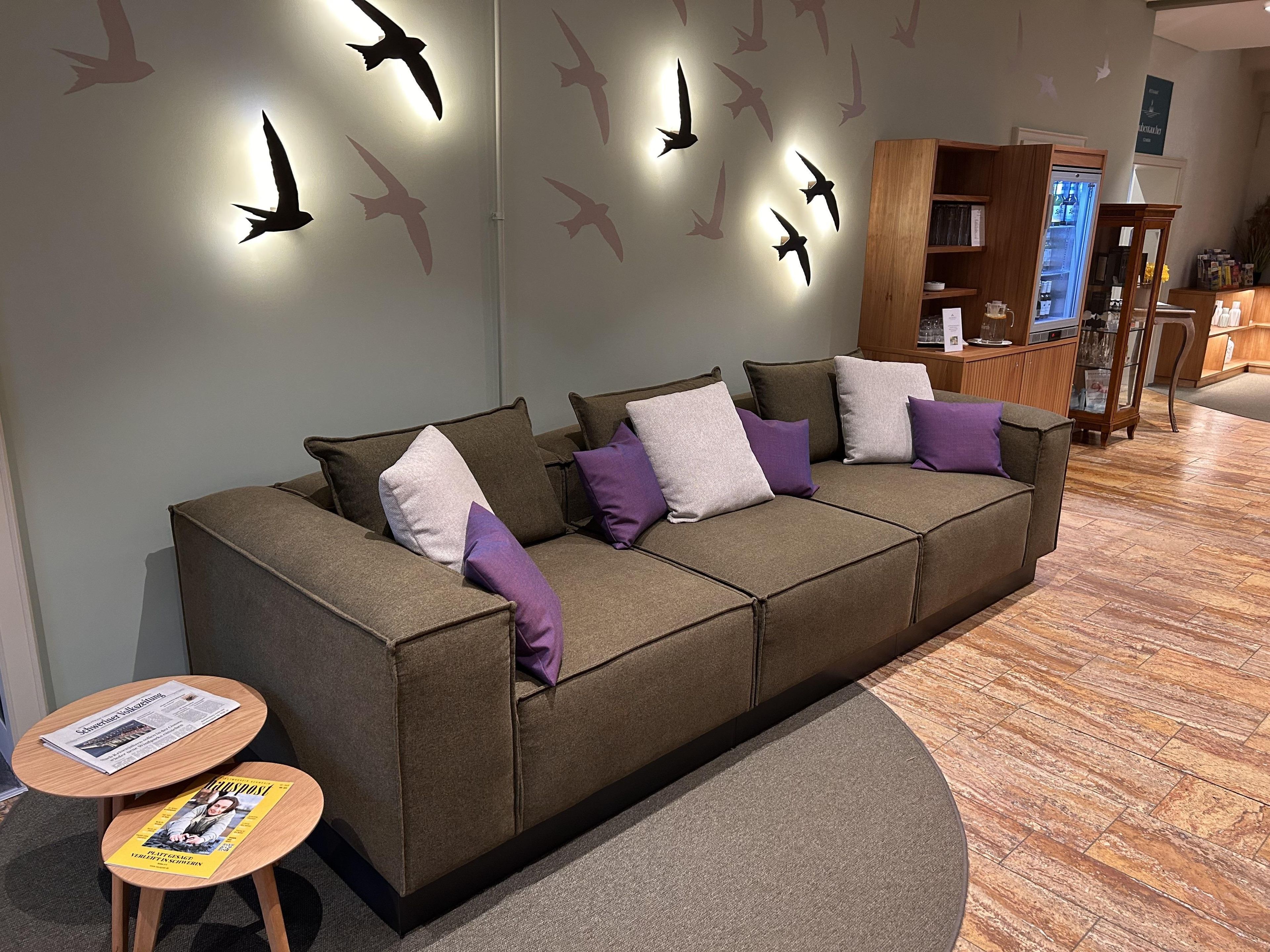 Een modern interieur met een bank, een klein tafeltje met een tijdschrift en een muur met silhouetten van vogels.