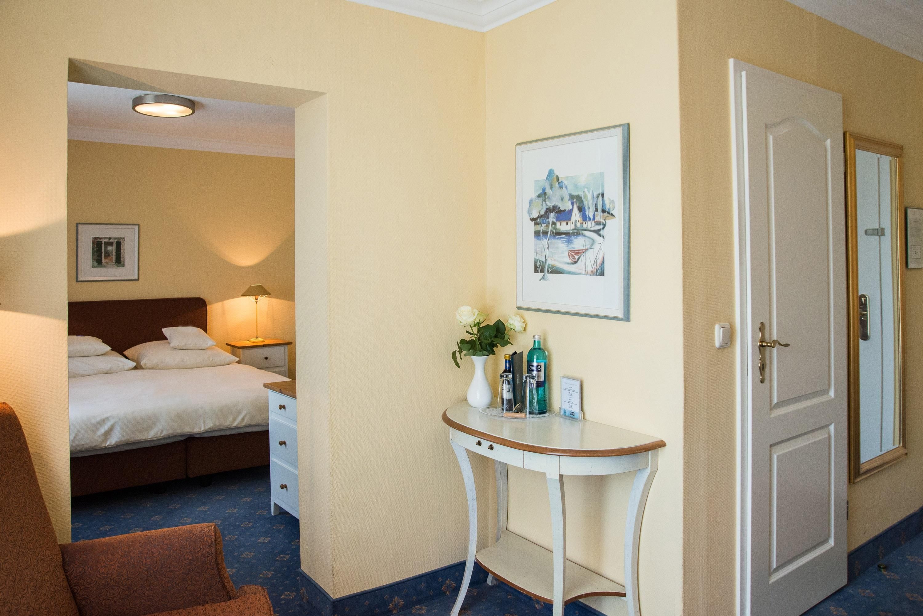A hotel room with a bed, bedside table, lamp, framed picture, and a door.