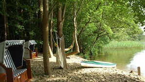 Une plage avec des hamacs et un bateau sur le sable, entourée d’arbres et d’eau.