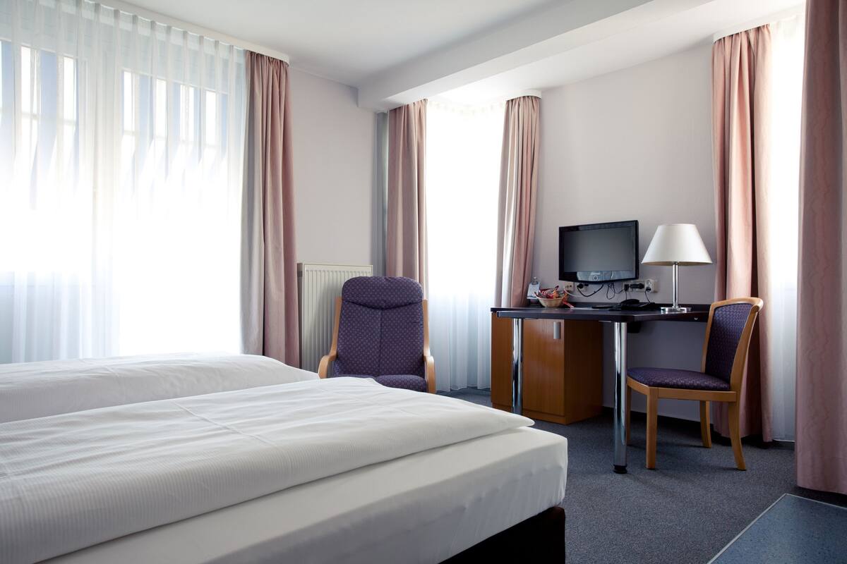 A hotel room with a large bed, a desk with a computer, two chairs, and a TV.