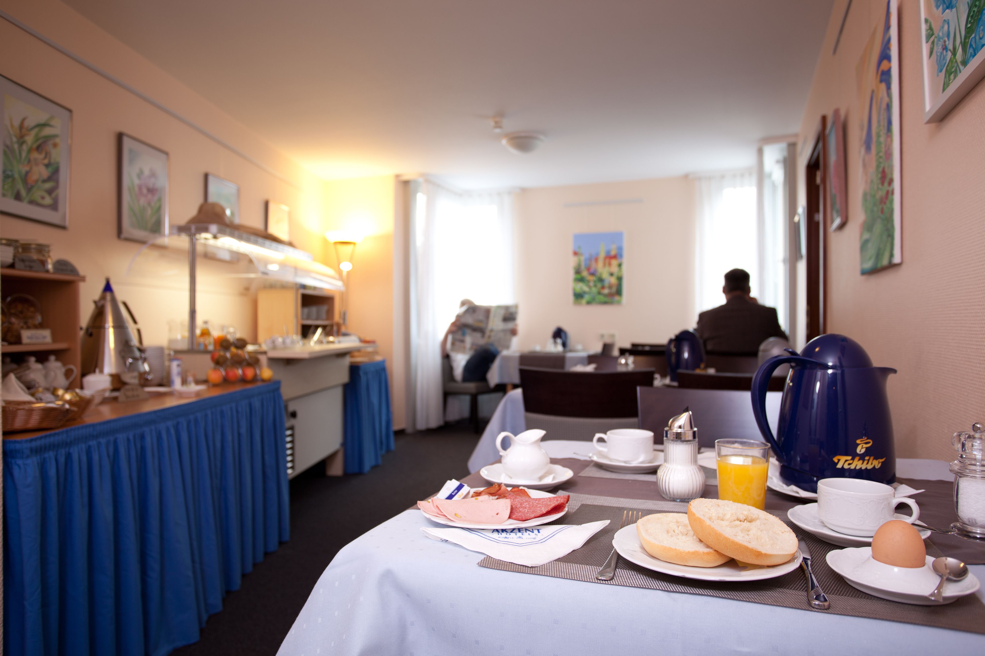 Preparación para el desayuno con una mesa, platos, tazas y una tetera en una habitación de hotel.