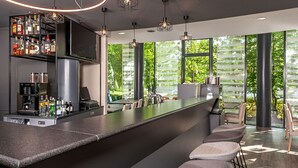 A modern bar area with a long counter, bar stools, and a variety of bottles and glasses. - NH München Unterhaching (Unterhaching)