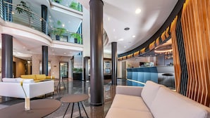 A modern lobby with a curved ceiling, a reception desk, a seating area with sofas and tables, and a bar area with wooden accents. - NH München Unterhaching (Unterhaching)