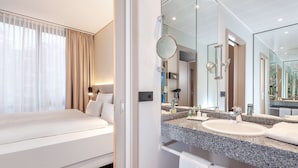 A modern hotel room with a large bed, a bathroom with a granite countertop, and a large mirror. - NH München Unterhaching (Unterhaching)