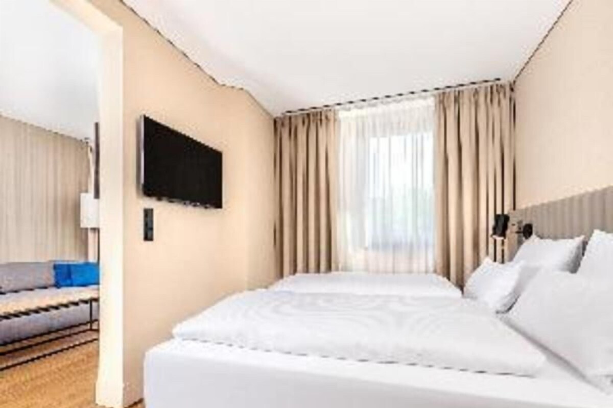 Habitación de hotel con cama, televisión y ventana con cortinas.