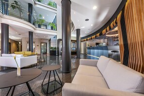 A modern lobby with a reception desk, seating area, and a staircase leading to upper floors. - NH München Unterhaching (Unterhaching)