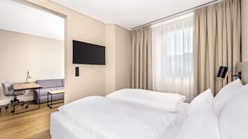 Ein Hotelzimmer mit einem Bett, einem Schreibtisch mit Stuhl, einem an der Wand befestigten Fernseher und einem Fenster mit Vorhängen.