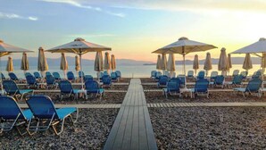 A beachside promenade with rows of blue lounge chairs and umbrellas, leading to a calm sea. - Alkyon Resort Hotel & Spa (Velo-Vocha)