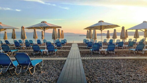 A beachside promenade with rows of blue lounge chairs and umbrellas, leading to a calm sea. - Alkyon Resort Hotel & Spa (Velo-Vocha)