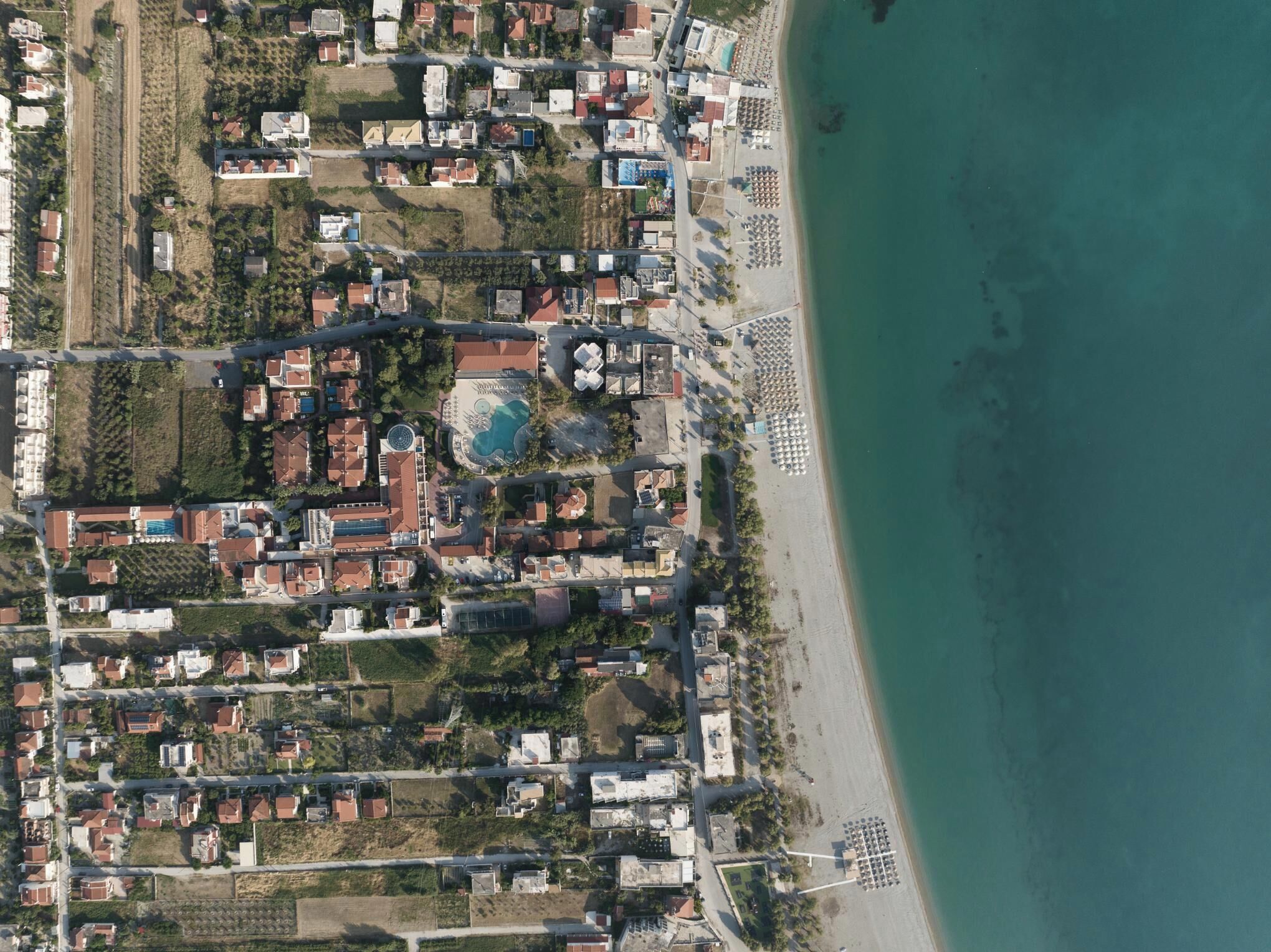 Luftaufnahme eines Küstenresorts mit Strand, Schwimmbad und mehreren Gebäuden.