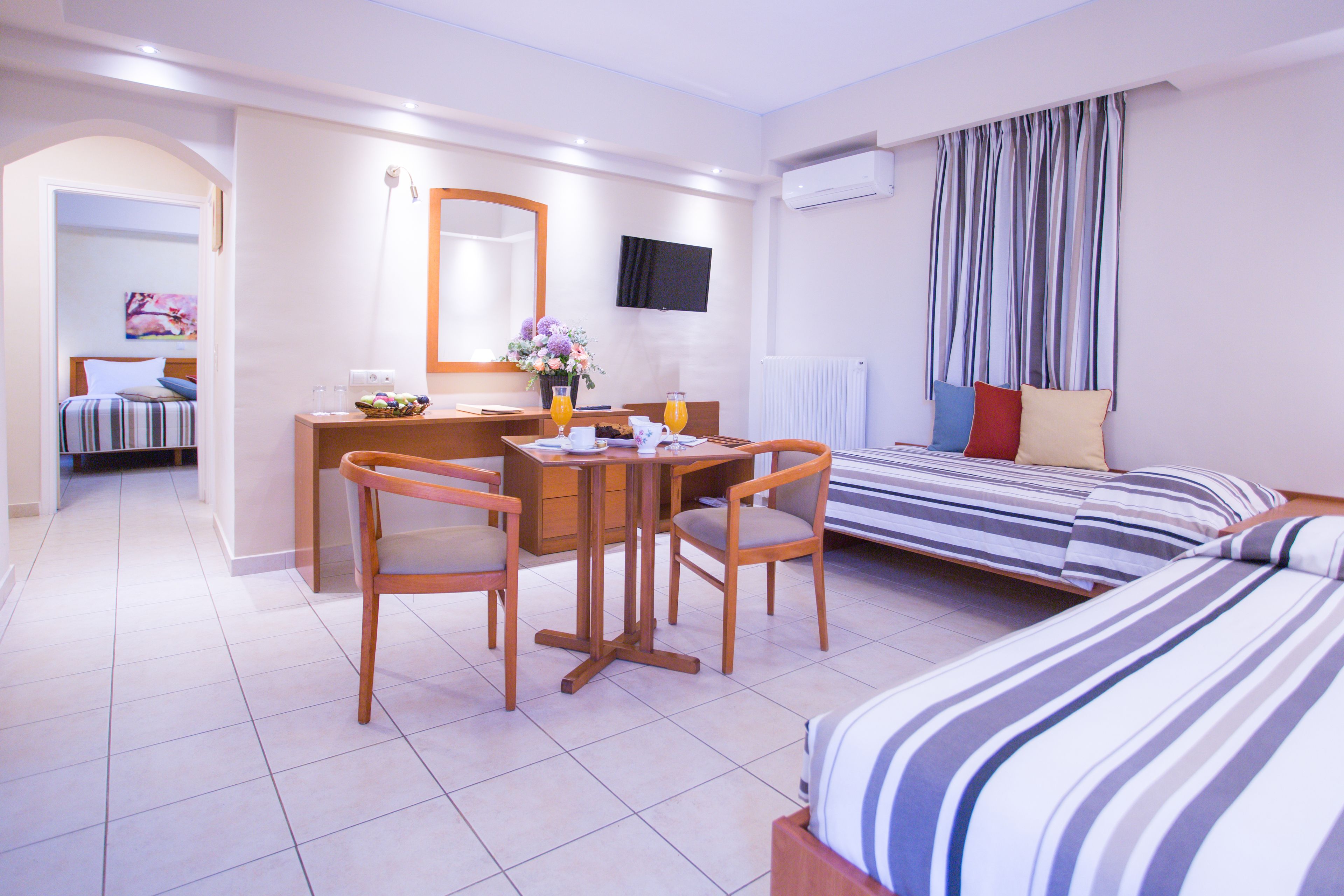 Een hotelkamer met een bed, een bureau met stoelen, een televisie en een raam met gordijnen.